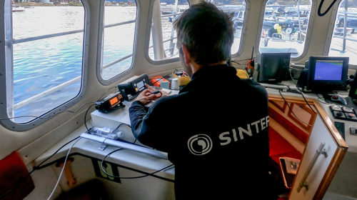 Styringsenheten plasseres i styrhuset av forsker Morten Steen Bondø. Den kobles mot sikkerhetsarmbåndet og Telenor Kystradio. Foto: SINTEF